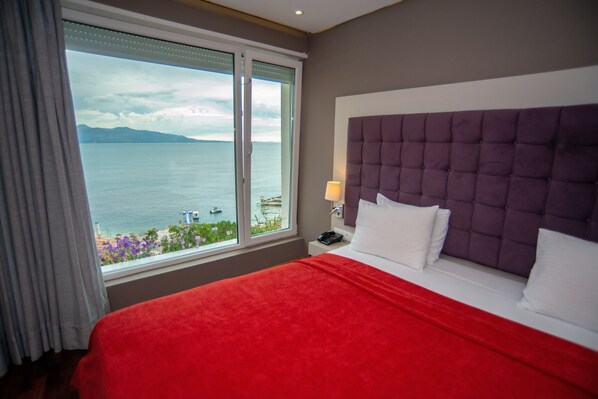 A hotel room with a large bed, a view of the sea, and a window with curtains.