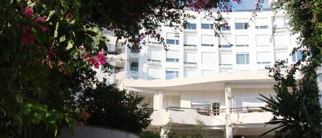 A modern building with a curved facade, surrounded by lush greenery and flowering plants.