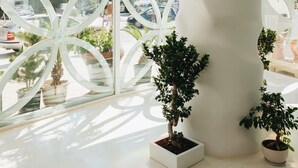 Un intérieur moderne avec une grande fenêtre ornée de motifs géométriques, des plantes en pot et un panneau indiquant la présence d’un restaurant.