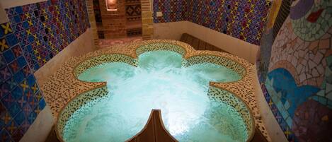 A hot tub with mosaic tile walls and a wooden deck.