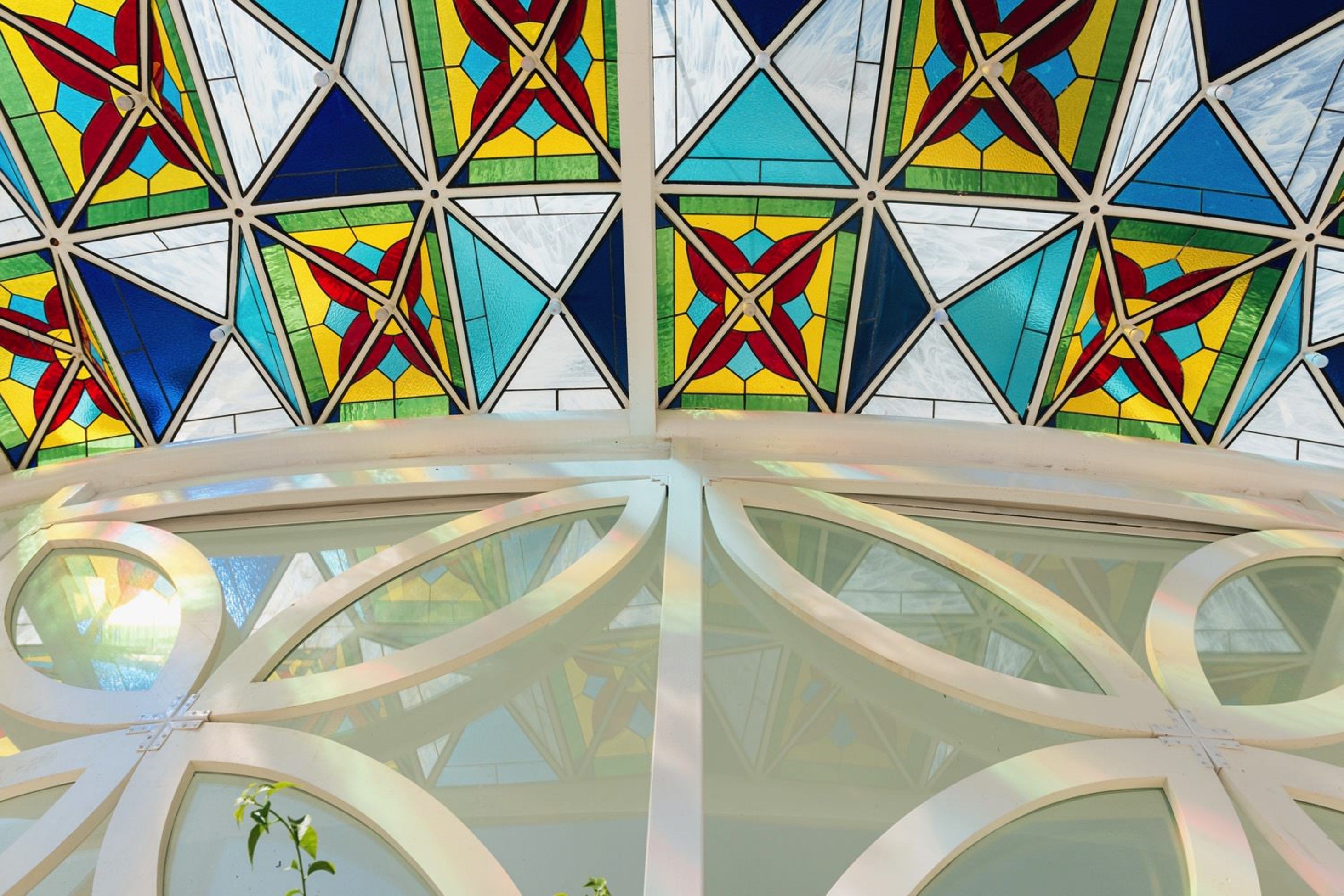 A stained glass ceiling with geometric patterns and a skylight with a plant.