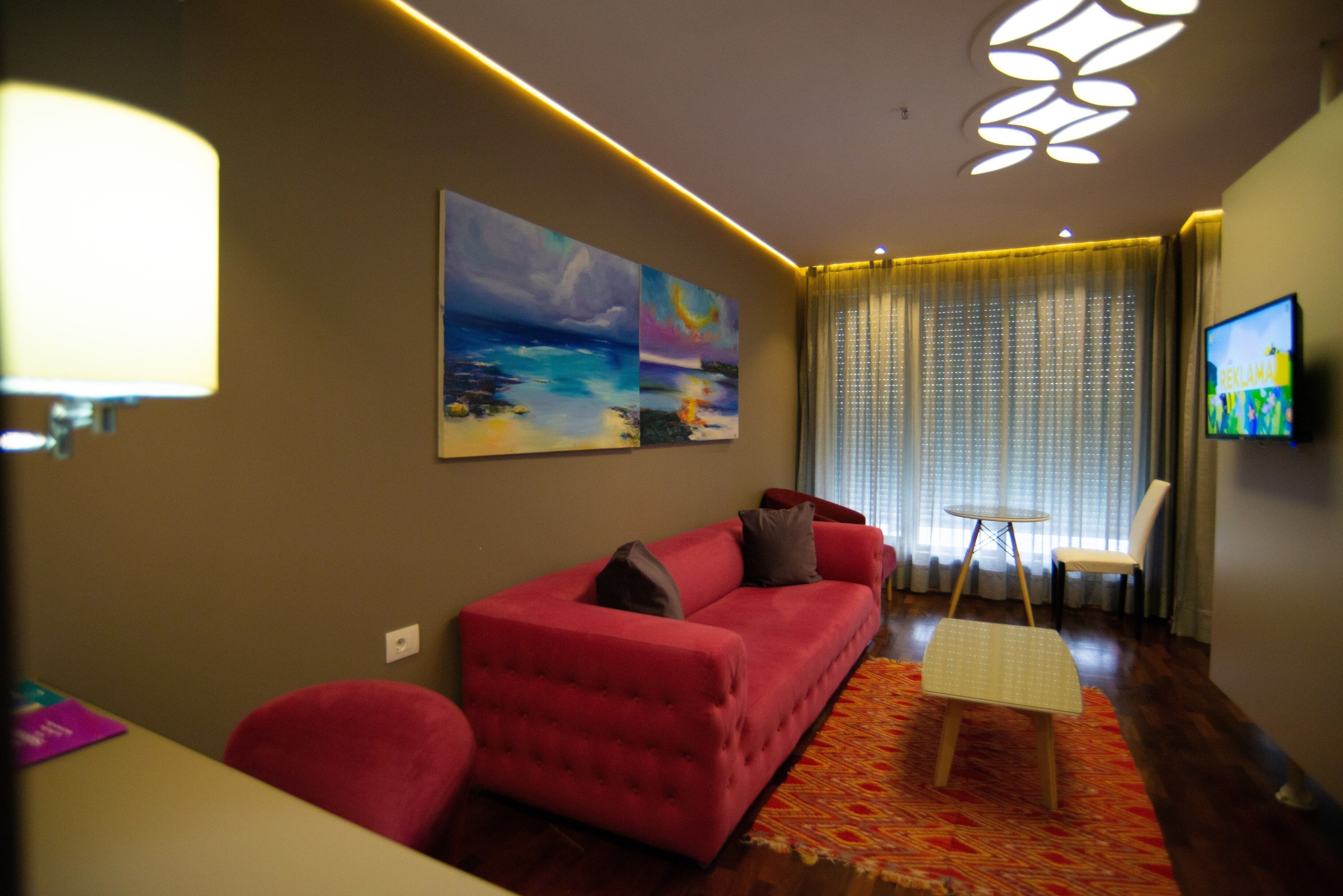 A modern living room with a red sofa, a small table, and a painting on the wall.