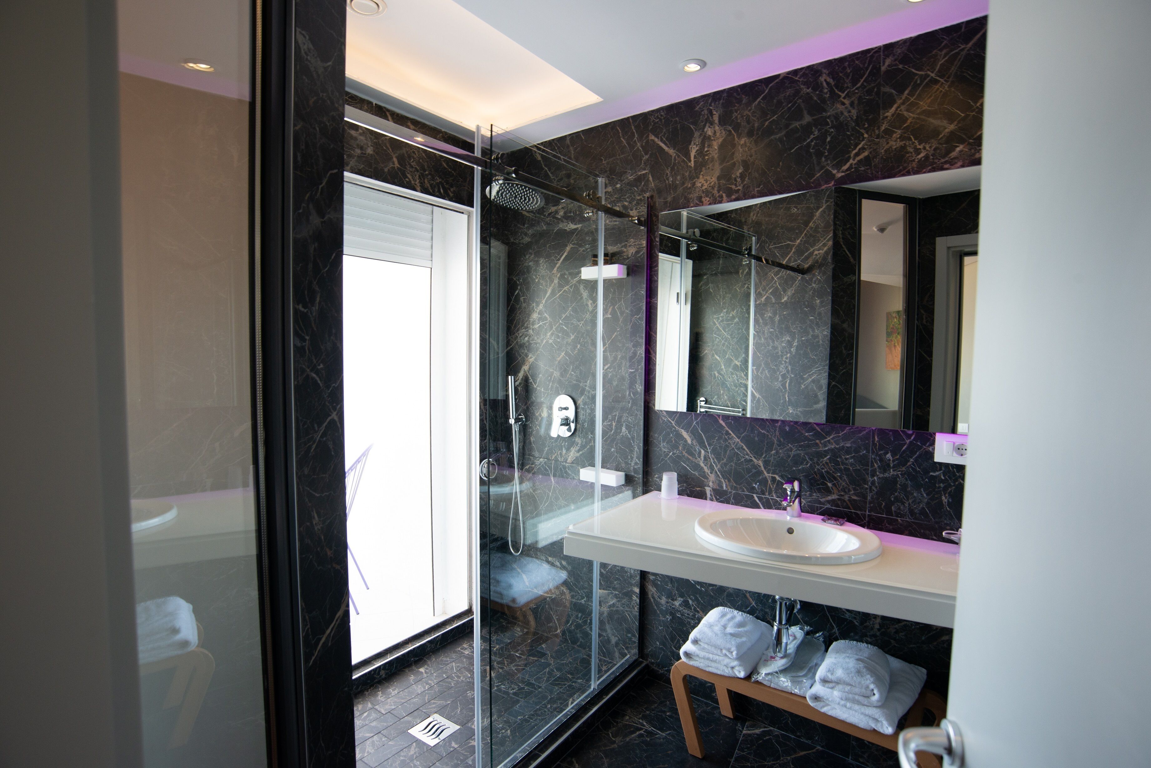 Un baño moderno con ducha envuelta en vidrio, lavamanos blanco y pared con azulejos de mármol.