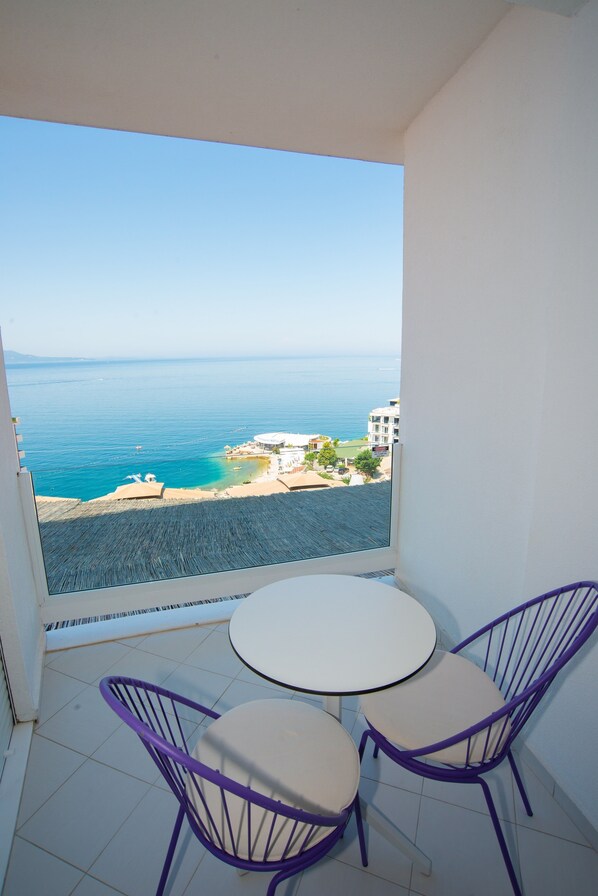 Un balcón con vistas al mar, una mesa redonda y dos sillas moradas.