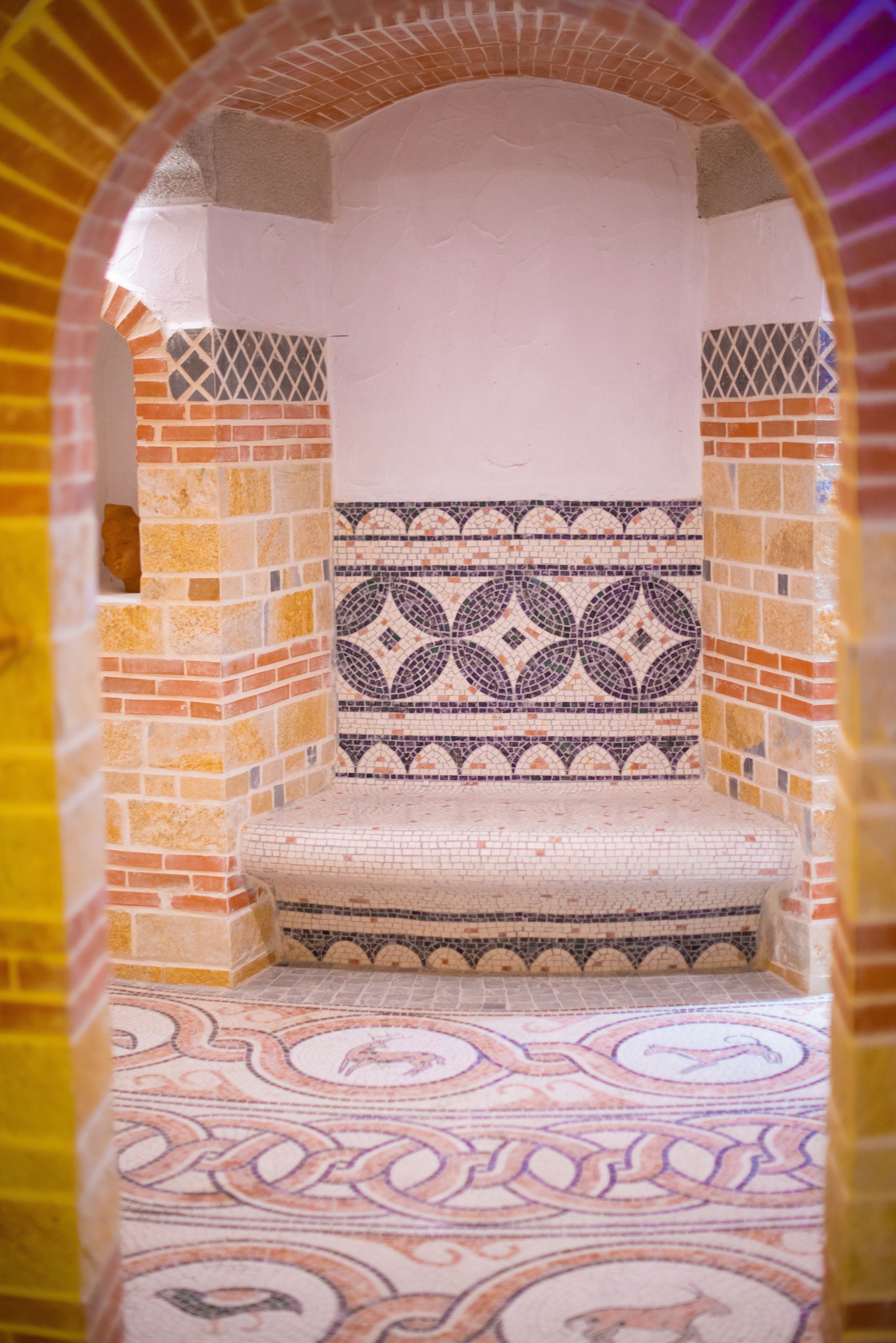 Una habitación con piso y paredes estampadas, un banco y un arco de entrada.