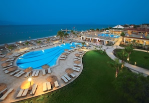 Un resort con una amplia piscina, tumbonas, sombrillas y vistas al mar.
