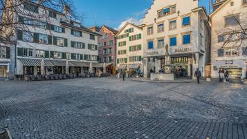 Una plaza adoquinada con mesas al aire libre y una fuente, rodeada de edificios históricos con tiendas.