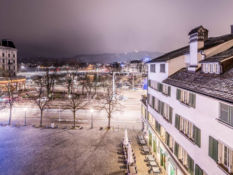 Un hotel con patio, mesas al aire libre y vista a la ciudad iluminada de noche.