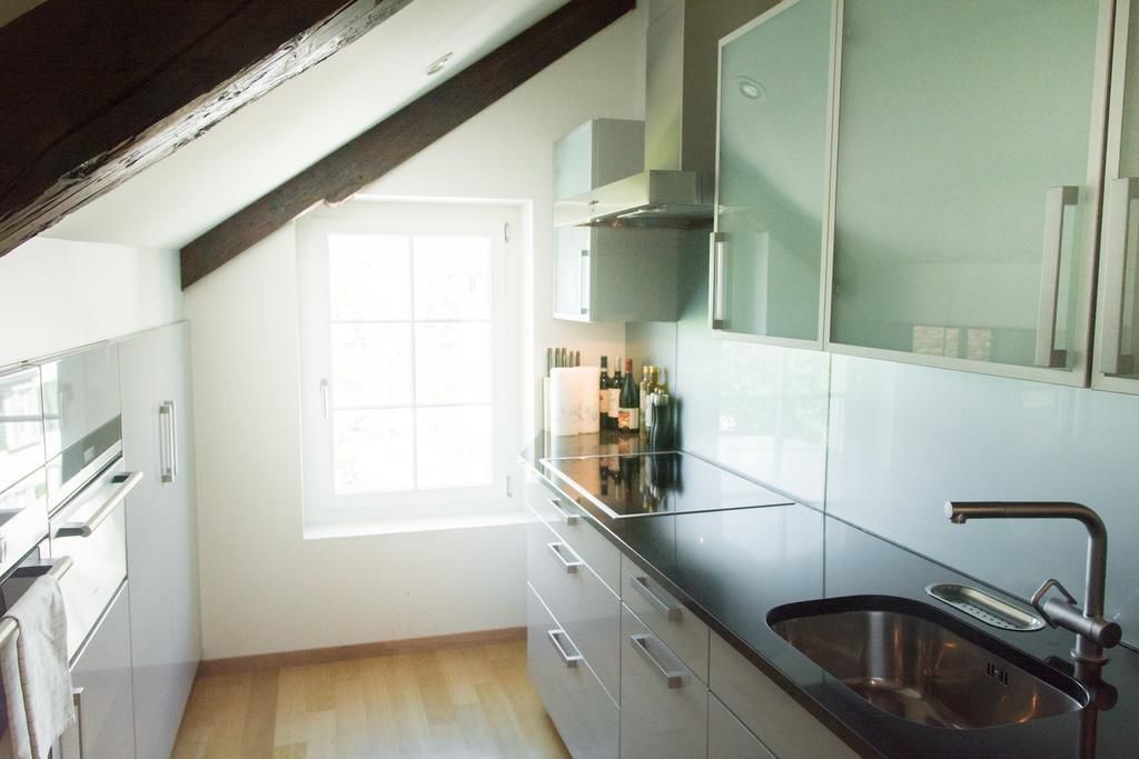 A modern kitchen with a large window, stainless steel appliances, and a wooden ceiling beam.