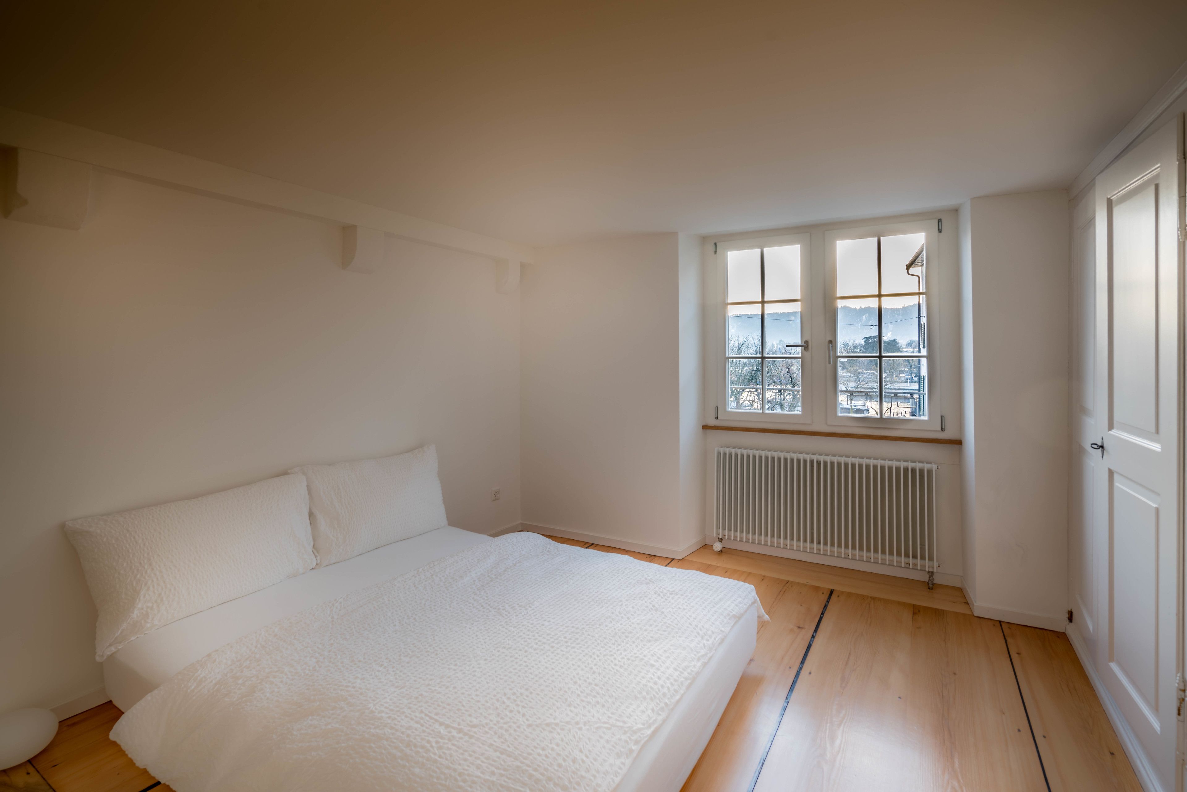 A bedroom with a large bed, a window with a view, and a radiator.