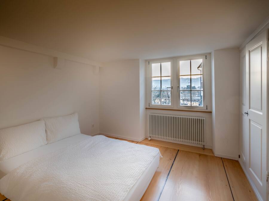 A bedroom with a large bed, a window with a view, and a radiator.