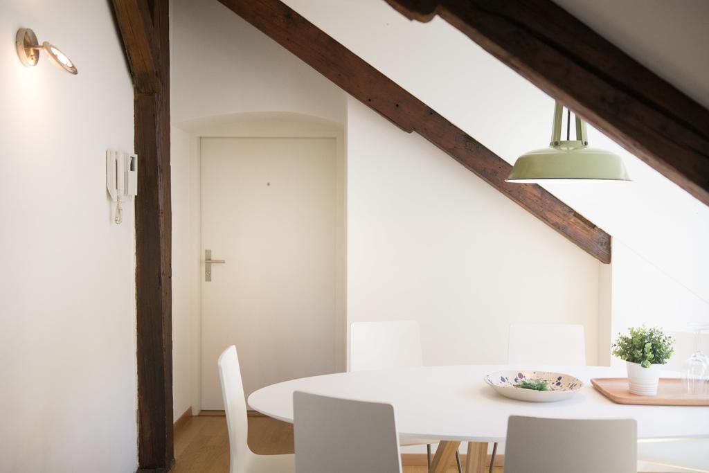 A dining area with a white table, chairs, a bowl, a potted plant, and a hanging light fixture.