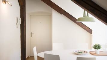 A dining area with a white table, chairs, a bowl, a potted plant, and a hanging light fixture.
