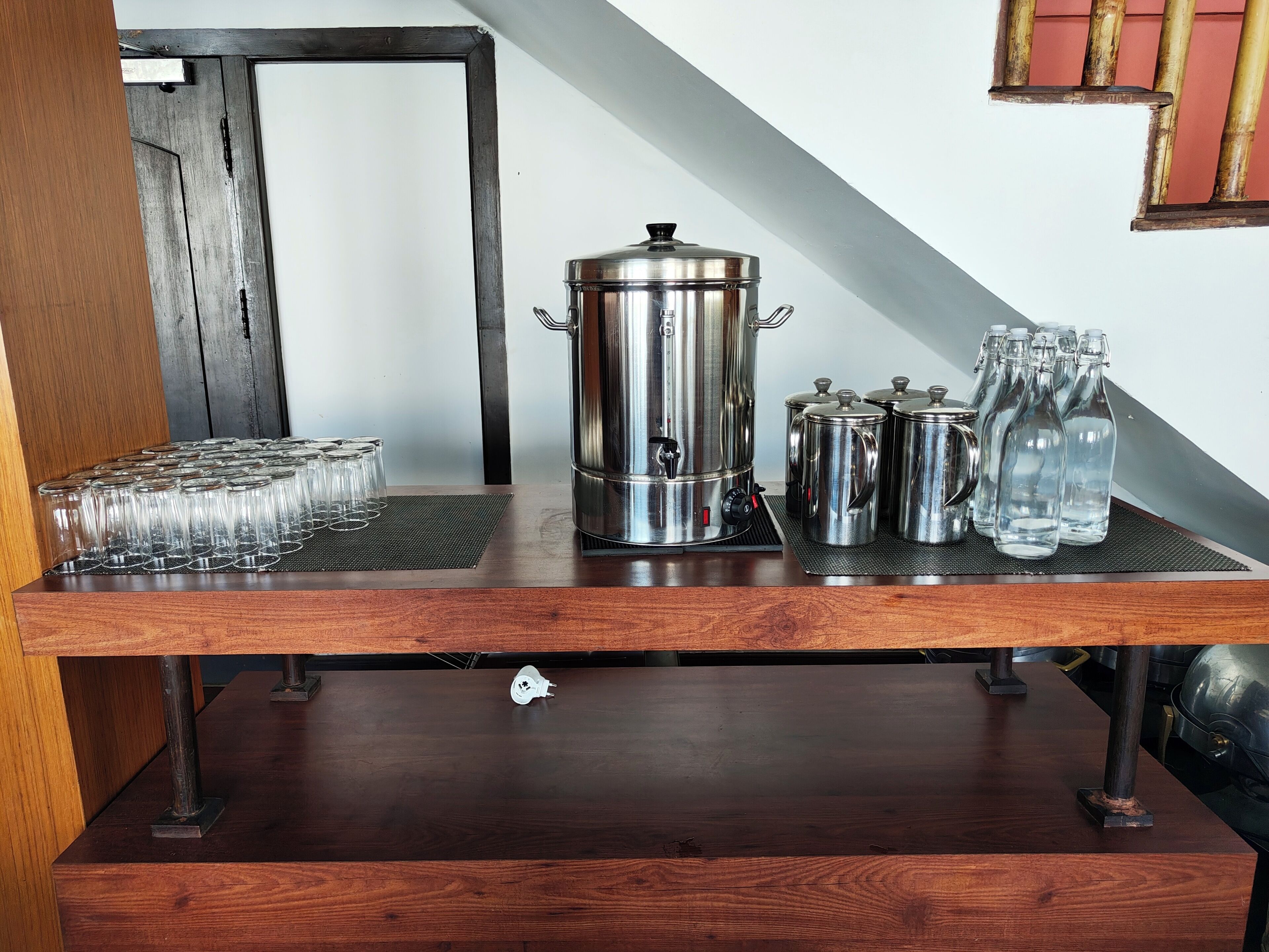 A wooden table with a coffee maker, several glass bottles, and a metal container.