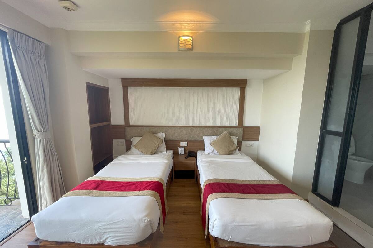 A hotel room with two beds, a large window, and a balcony.