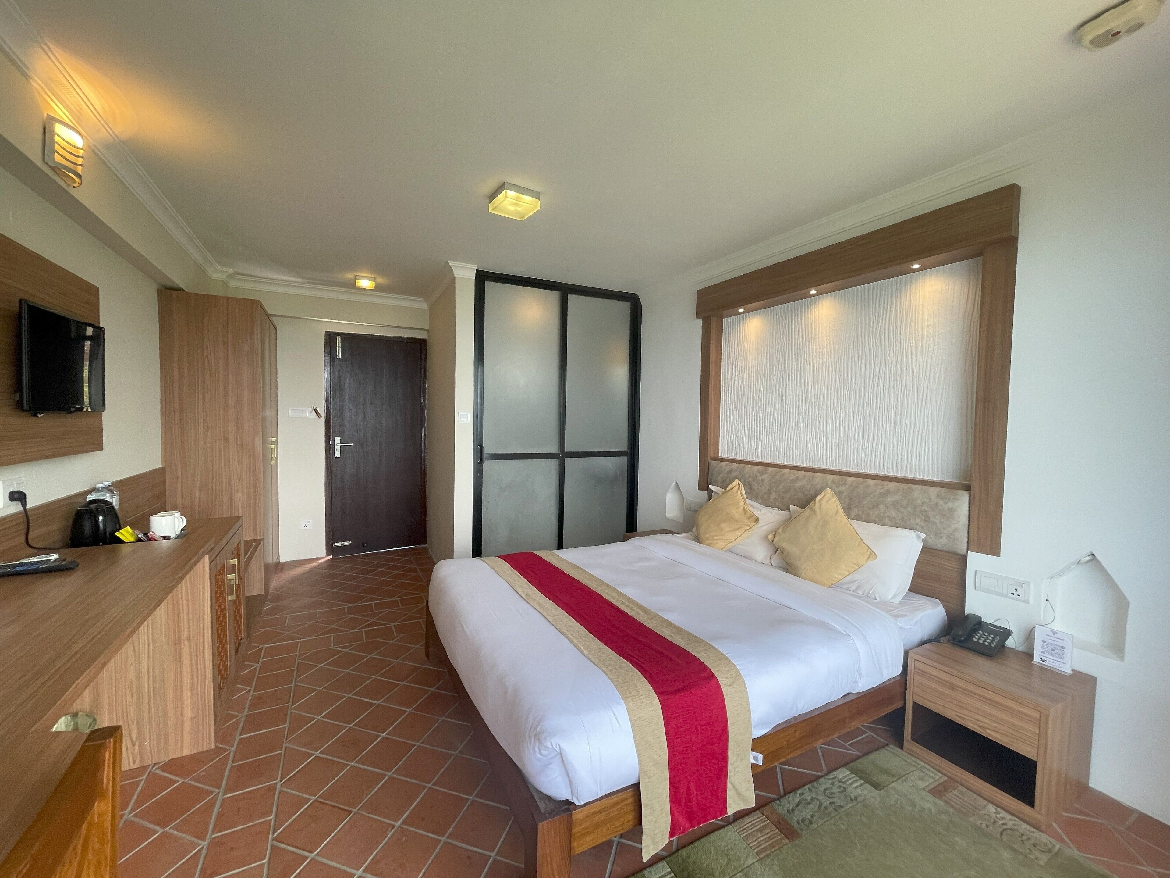 A hotel room with a large bed, a desk with a coffee maker, a TV, and a sliding door closet.