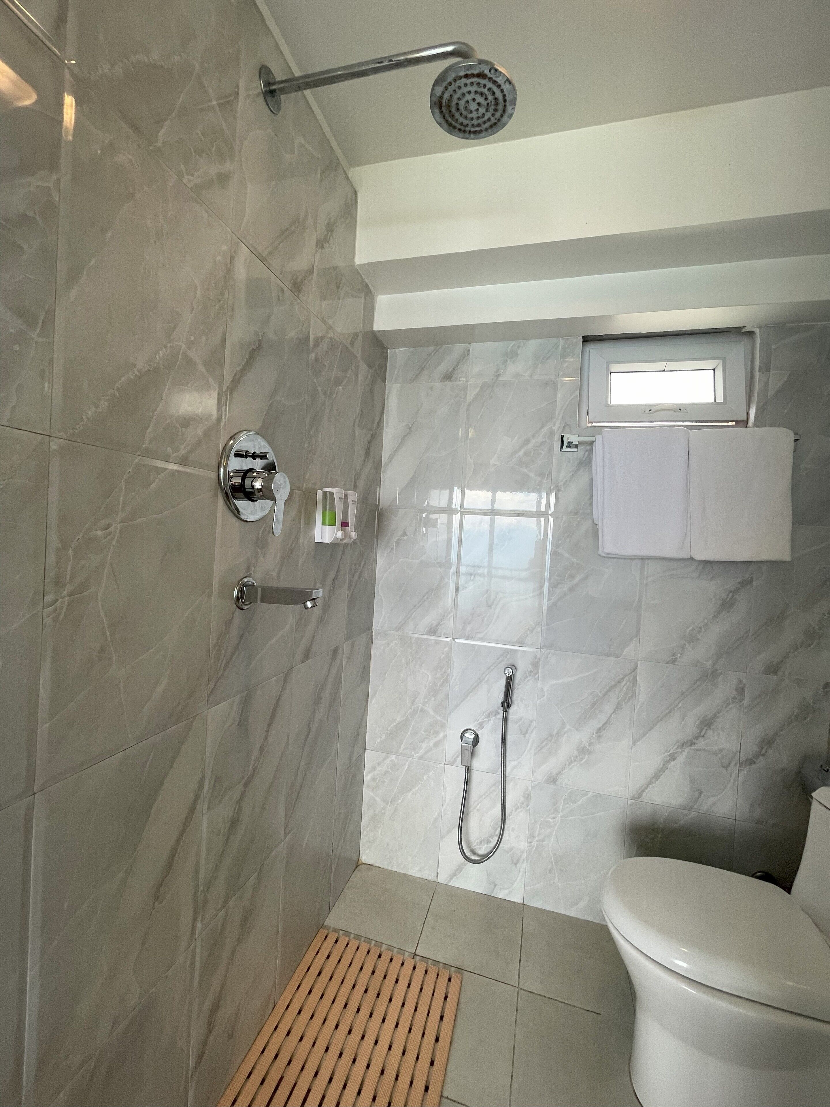 A bathroom with a shower, toilet, and a small window.