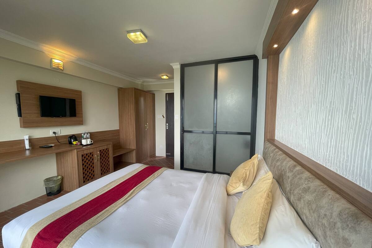 A hotel room with a bed, a TV mounted on the wall, a wooden wardrobe, and a sliding door.