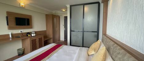 A hotel room with a bed, a TV mounted on the wall, a wooden wardrobe, and a sliding door.