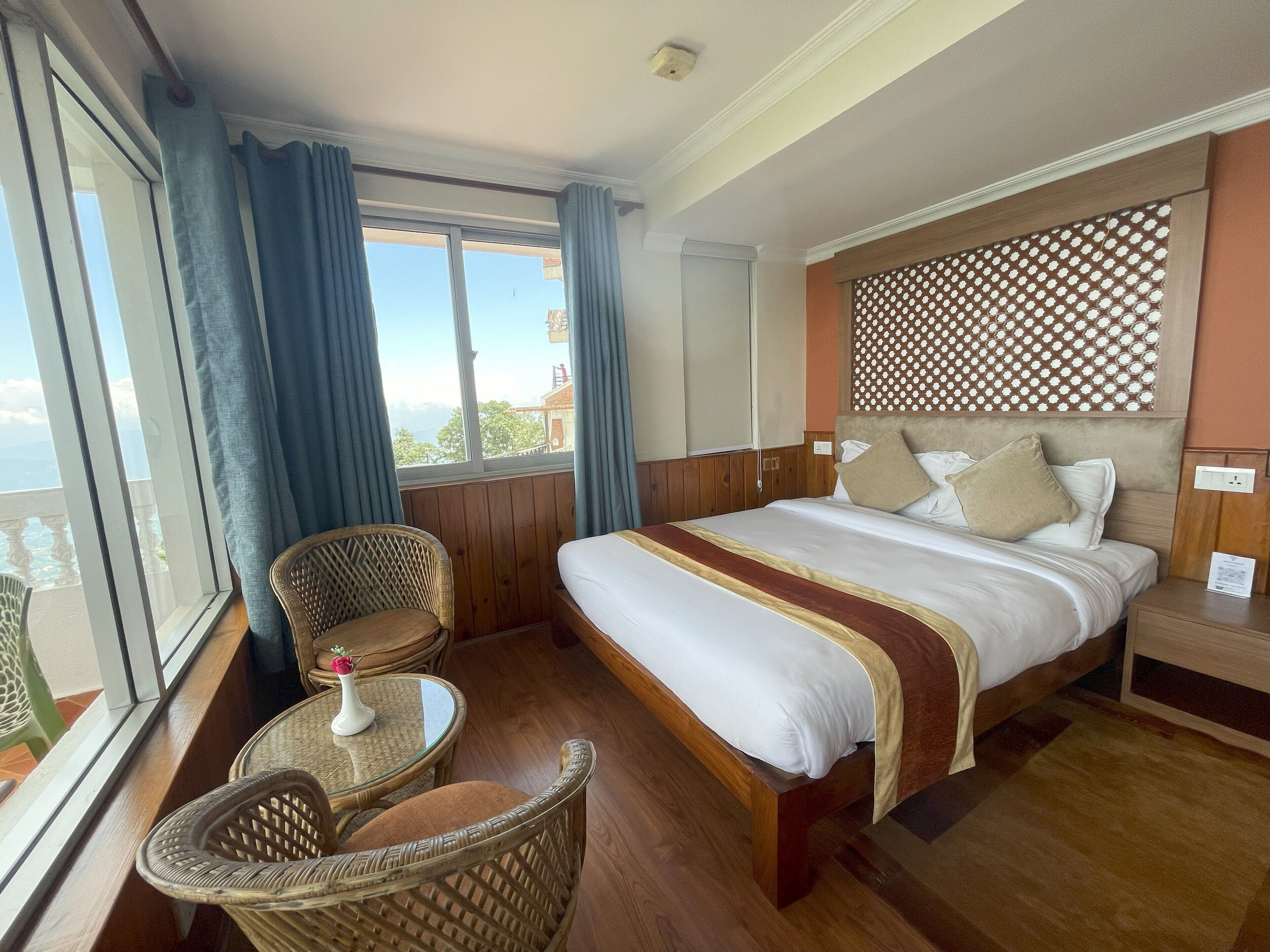 A hotel room with a large bed, a small round table, wicker chairs, and a view of the outdoors.