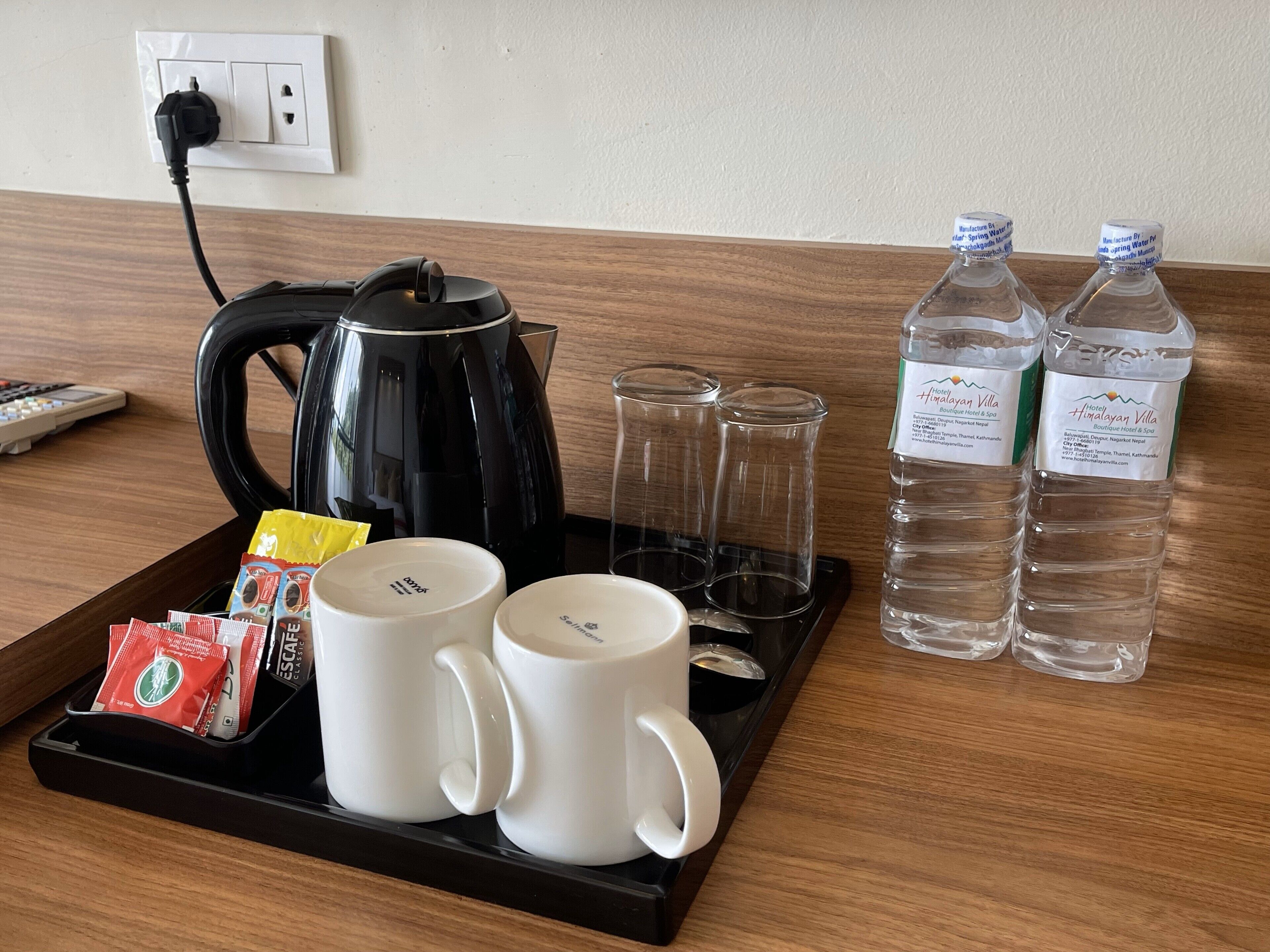 A hotel room's breakfast tray with a black electric kettle, two white mugs, two clear glasses, two bottles of water, and packets of tea and coffee.