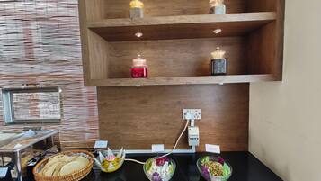 A buffet setup with various food items and a wooden shelf with jars.
