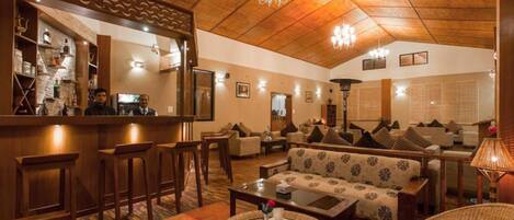 A hotel lobby with a wooden ceiling, bar area, sofas, and a round table with a vase.