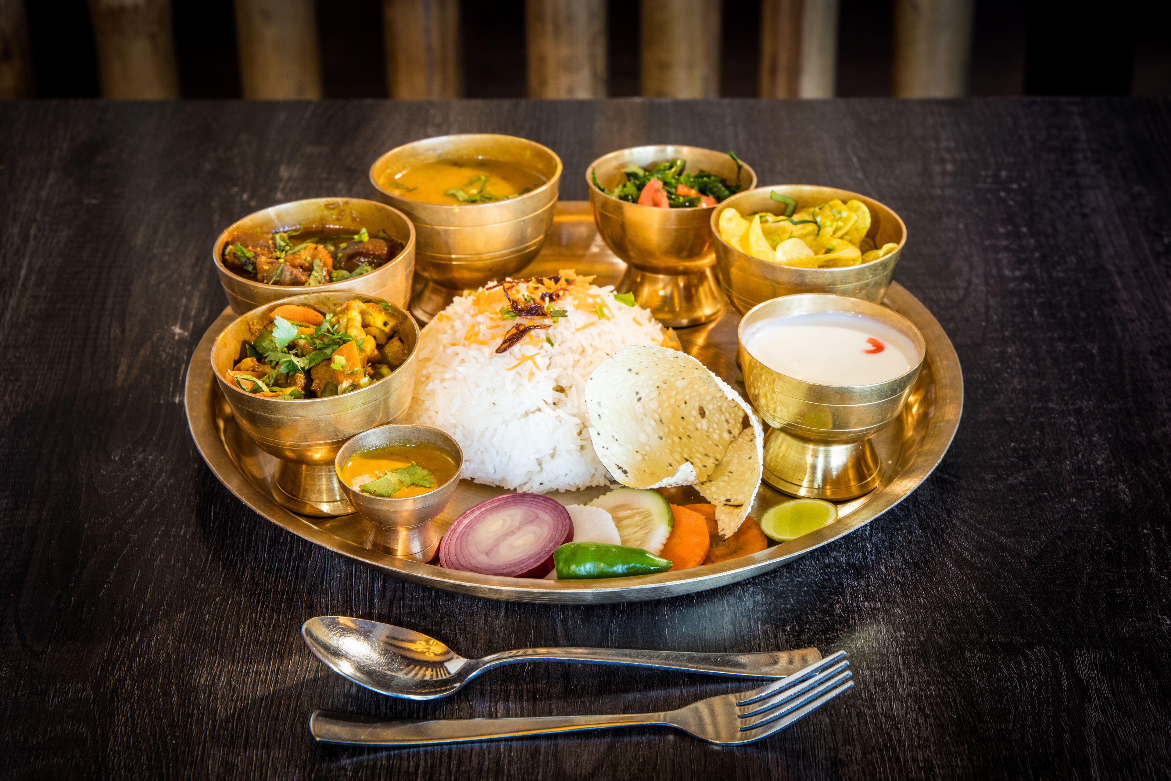 A traditional Indian meal on a metal tray with rice, various curries, and a bowl of yogurt.