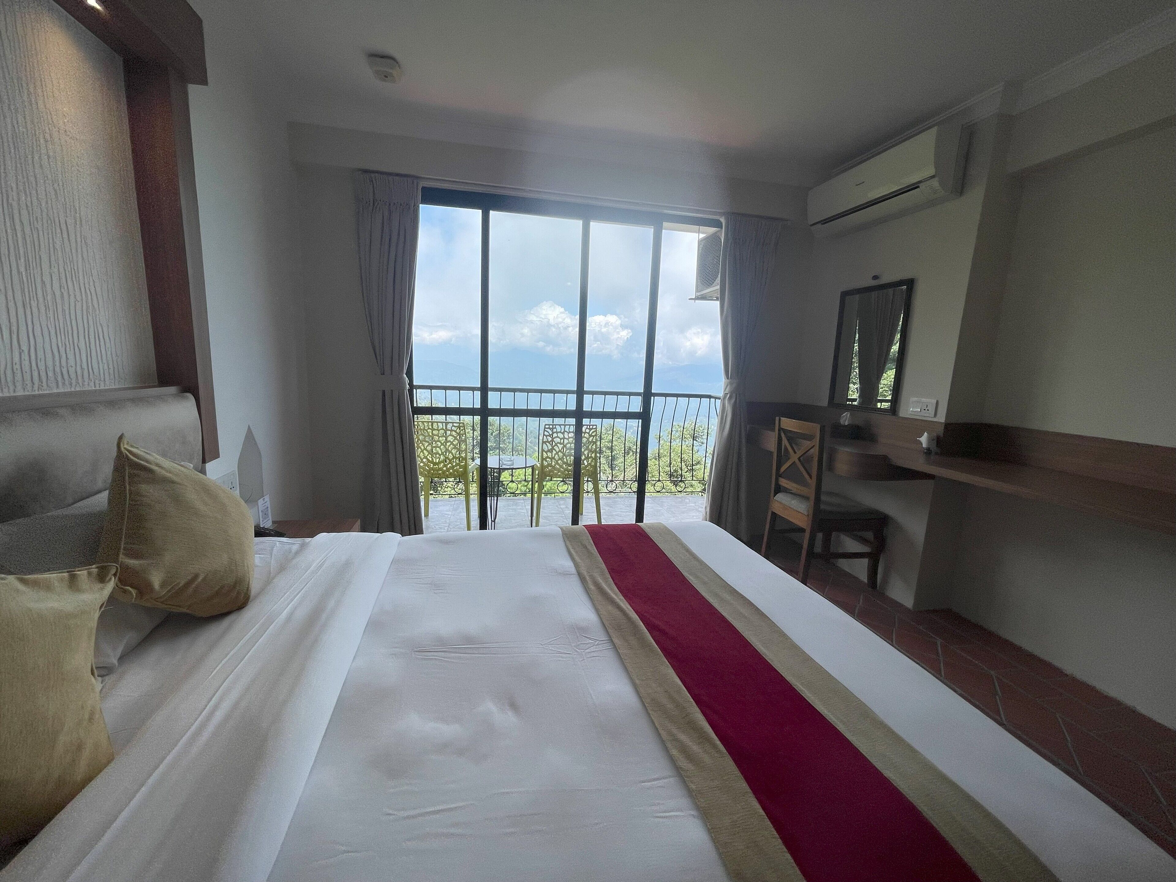 A hotel room with a large bed, a desk, and a balcony with a view.