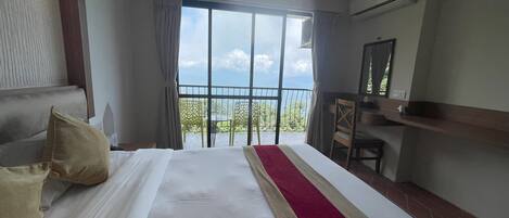 A hotel room with a large bed, a desk, and a balcony with a view.