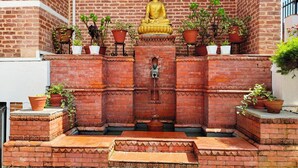 A golden Buddha statue on a brick platform with steps leading up to it, surrounded by potted plants. - Hotel Himalayan Villa - Nagarkot (Shankharapur)