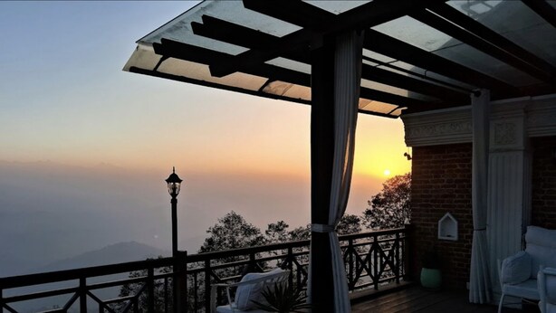 A wooden deck with outdoor seating, a pergola, and a view of the sunset over a mountainous landscape. - Hotel Himalayan Villa - Nagarkot (Shankharapur)