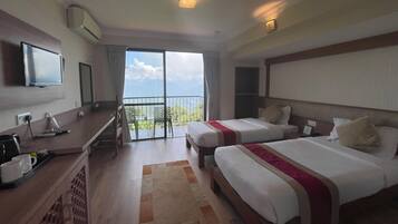 Habitación de hotel con dos camas, un escritorio con ordenador, televisor y balcón con vistas.
