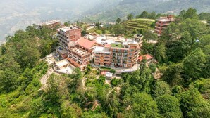 A multi-story building with a red roof, surrounded by lush greenery and hills in the background. - Hotel Himalayan Villa - Nagarkot (Shankharapur)