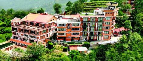 A multi-story hotel with balconies, surrounded by lush greenery and terraced fields.