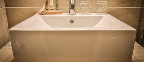 Un lavabo de baño rectangular con un grifo moderno, tres botellas de jabón líquido y dos vasos de cristal.