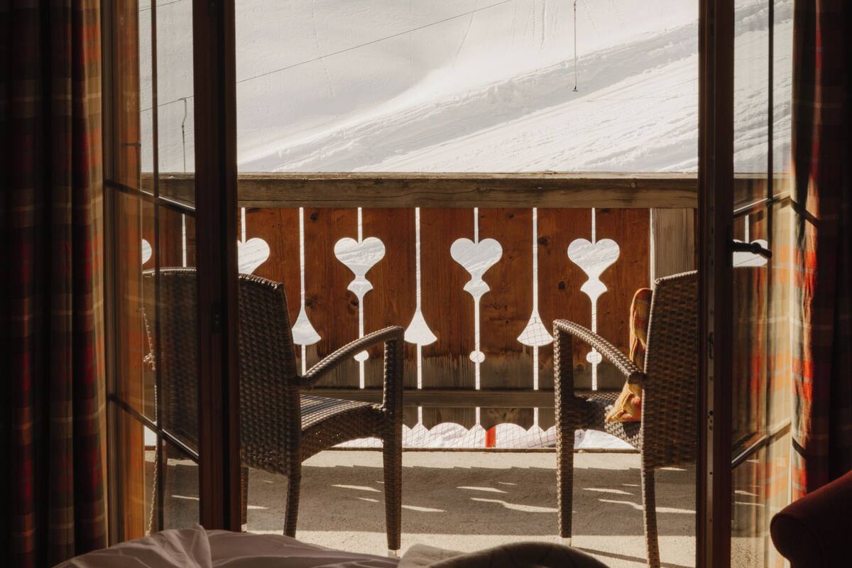 A room with a bed, two wicker chairs, and a window with a view of a snowy landscape.