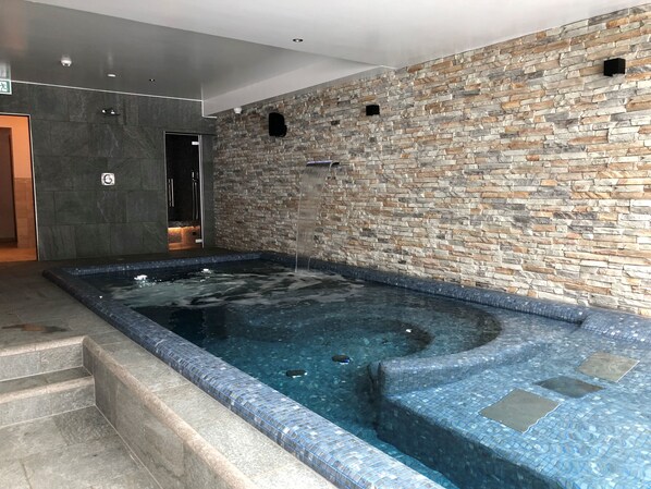 A spa area with a stone wall, a hot tub, and a shower area. - Mountain Lodge & Spa Les Crosets (Val d'Illiez)