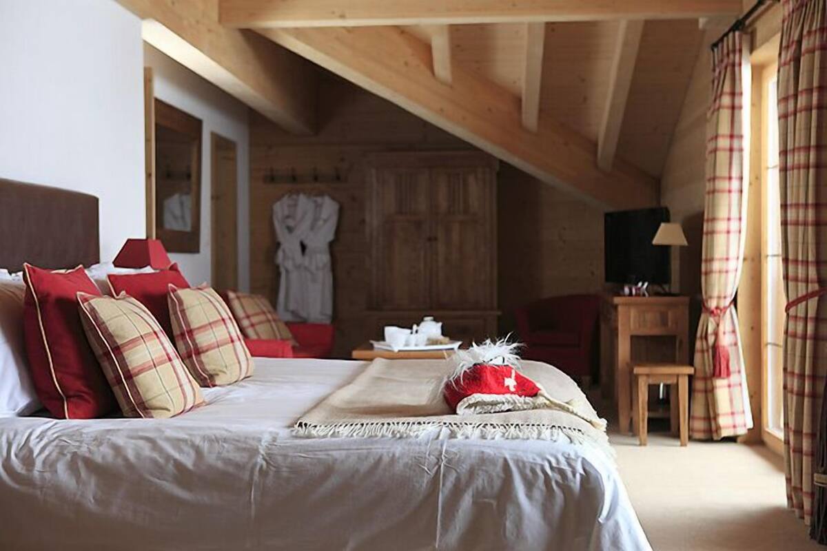 A bedroom with a bed, pillows, a bedside table, a chair, and a wooden ceiling.
