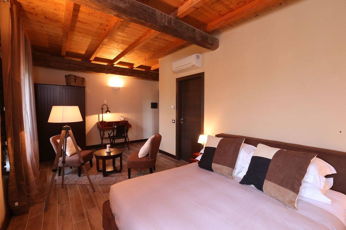 Une chambre d’hôtel avec un plafond en bois, un lit avec plusieurs oreillers, un bureau avec une lampe et une chaise.