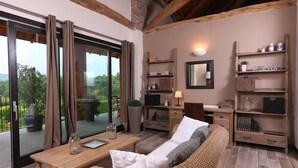 Una habitación acogedora con un amplio ventanal corredera que da a un balcón, mobiliario de mimbre, una mesa de madera y estantes con diversos objetos.