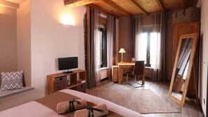 Habitación de hotel con cama, escritorio, silla, televisor y un espejo grande.