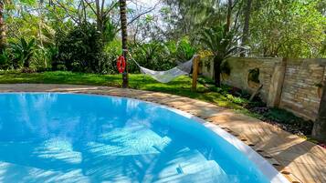 Una piscina rodeada de abundante vegetación y una hamaca.