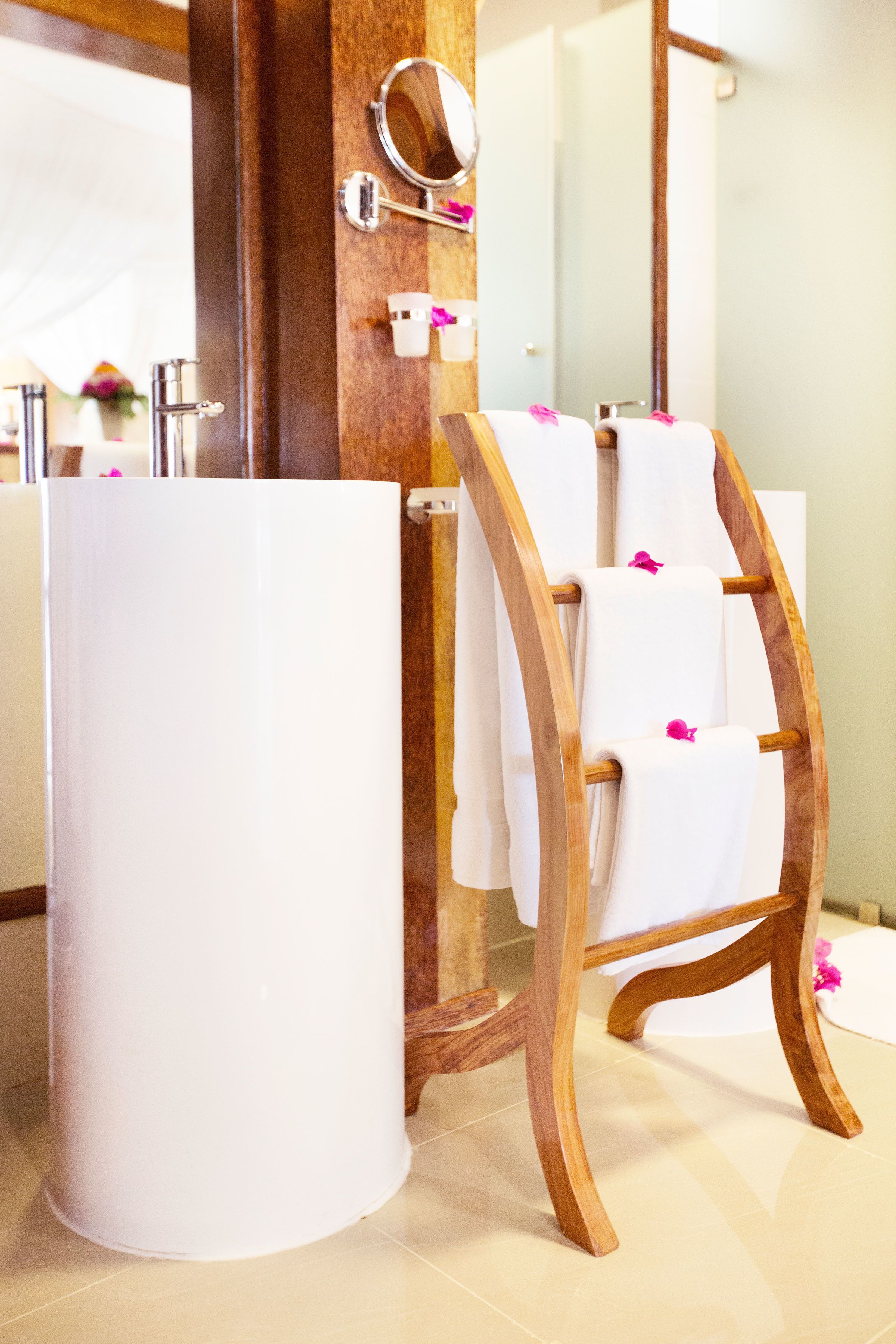 A bathroom with a wooden towel rack holding white towels, a large mirror, and a white sink.