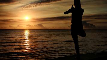 A silhouette of a person practicing yoga on a beach at sunset.