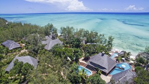 Una località turistica tropicale con diverse case vacanza coperte di paglia, una piscina e vista sul mare turchese.