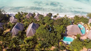 Una località turistica con bungalow a tetto di paglia, una piscina e vista sulla spiaggia.