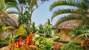 Un giardino tropicale con capanne a tetto di paglia, vegetazione lussureggiante e cielo sereno.