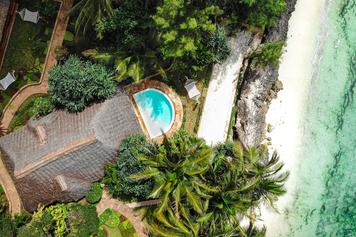 An aerial view of a resort with a swimming pool surrounded by lush greenery and a beach.