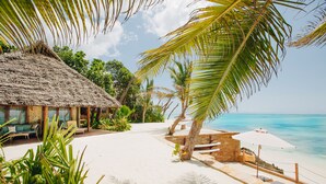 A beach with a thatched-roof hut, lounge chairs, and a palm tree. - Tulia Zanzibar Unique Beach Resort (Pongwe)
